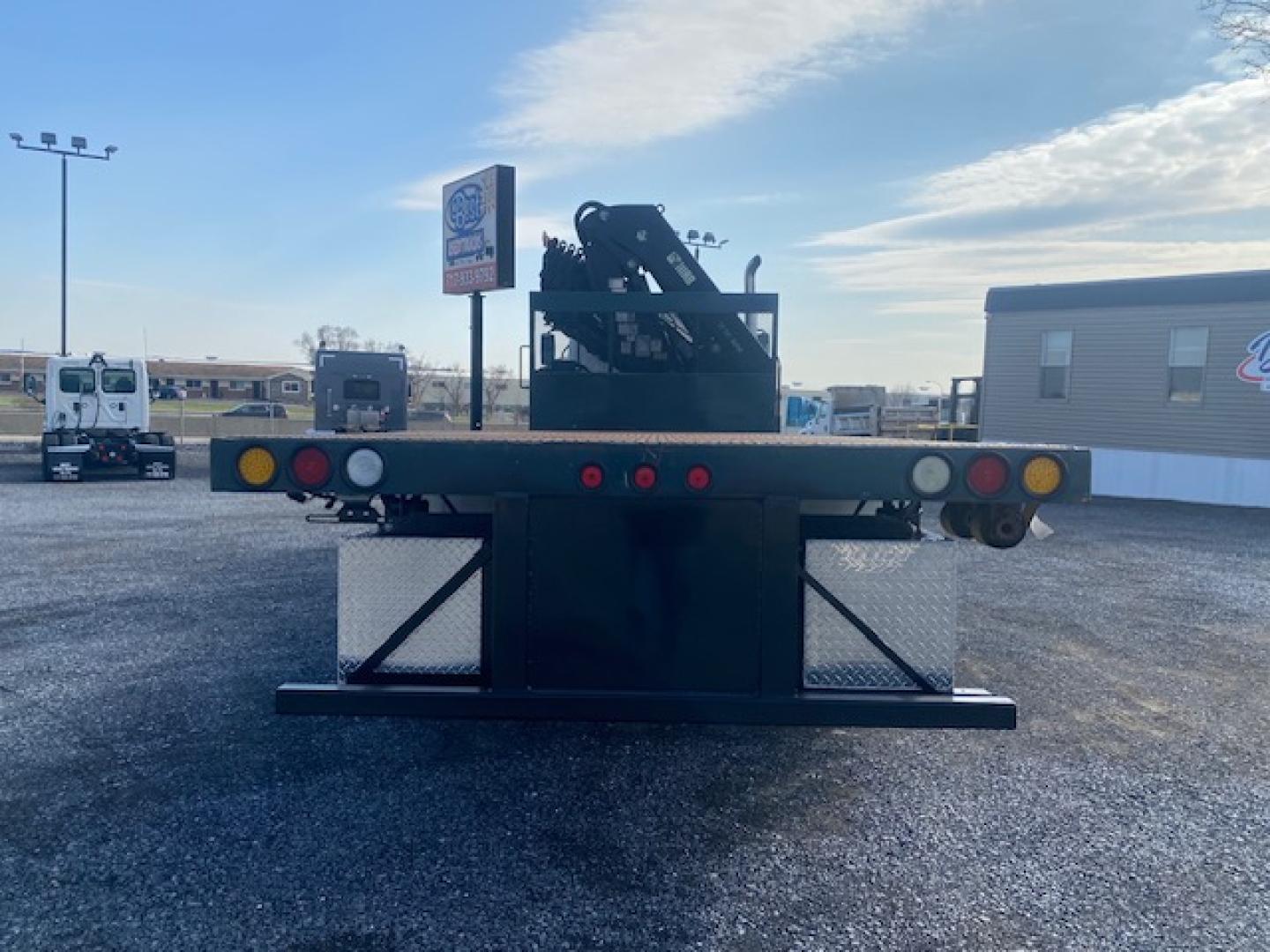 Freightliner M2-112 rear view showing flatbed trailer with hydraulic crane accessory and tail lights.