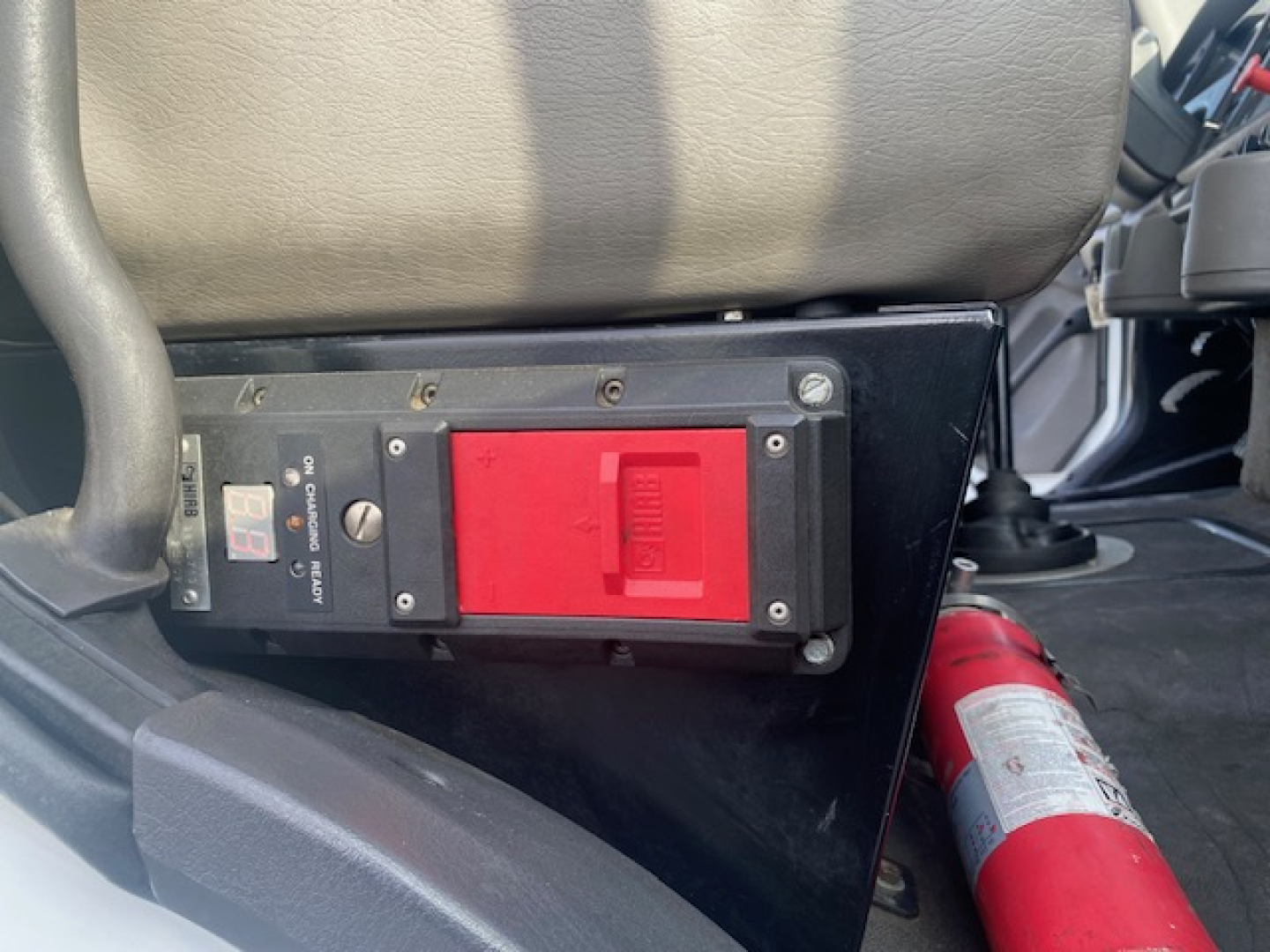 Cab interior showing a red switch panel and emergency fire extinguisher with labels, mounted under seat area.