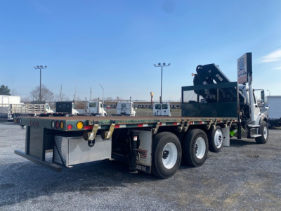 Flatbed tow truck with crane equipment on Freightliner M2-112 chassis, side view showing dual rear axles and long flatbed.