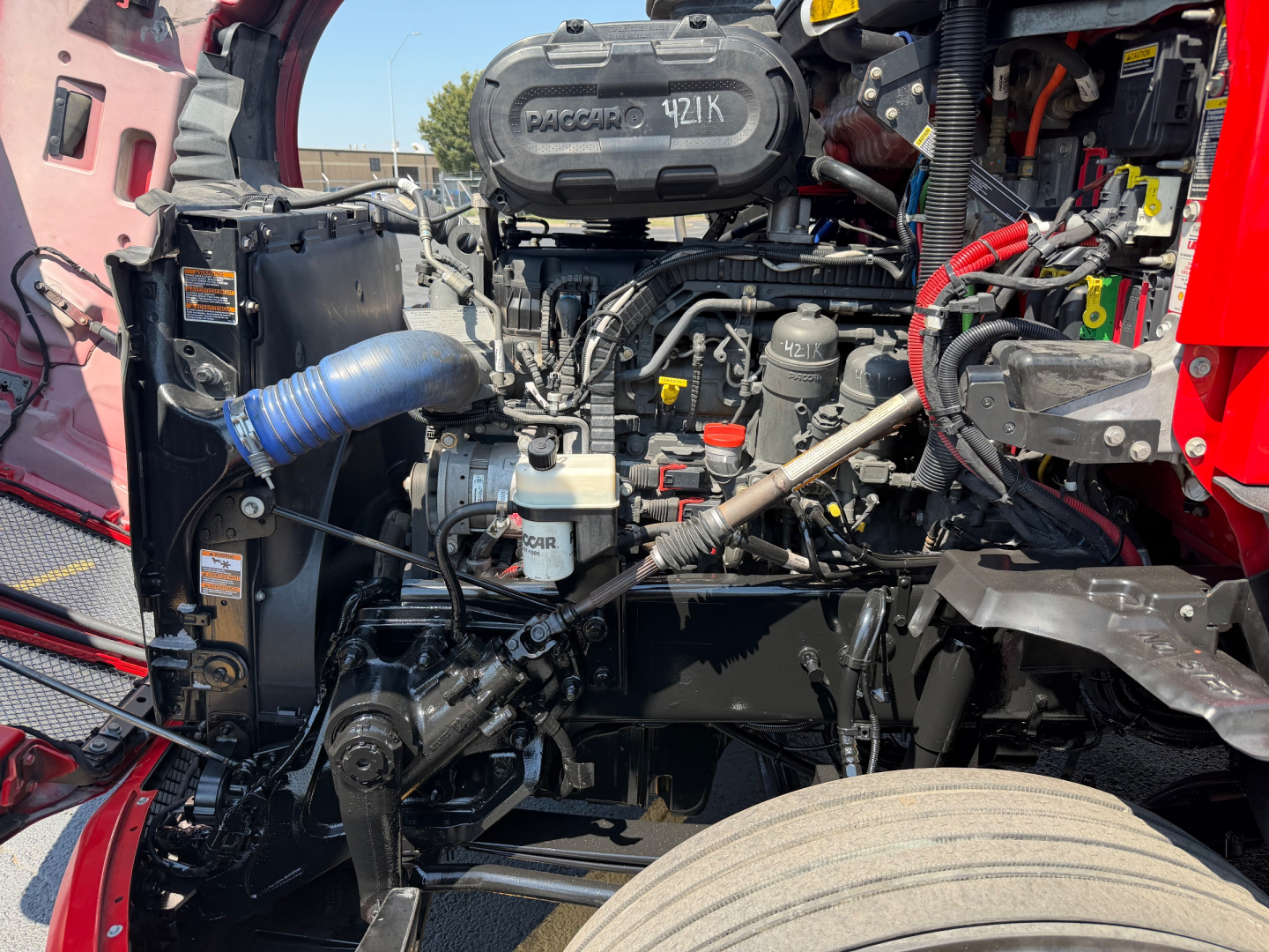 Kenworth T680 engine bay view showing engine components, hoses, and labels in the front compartment.