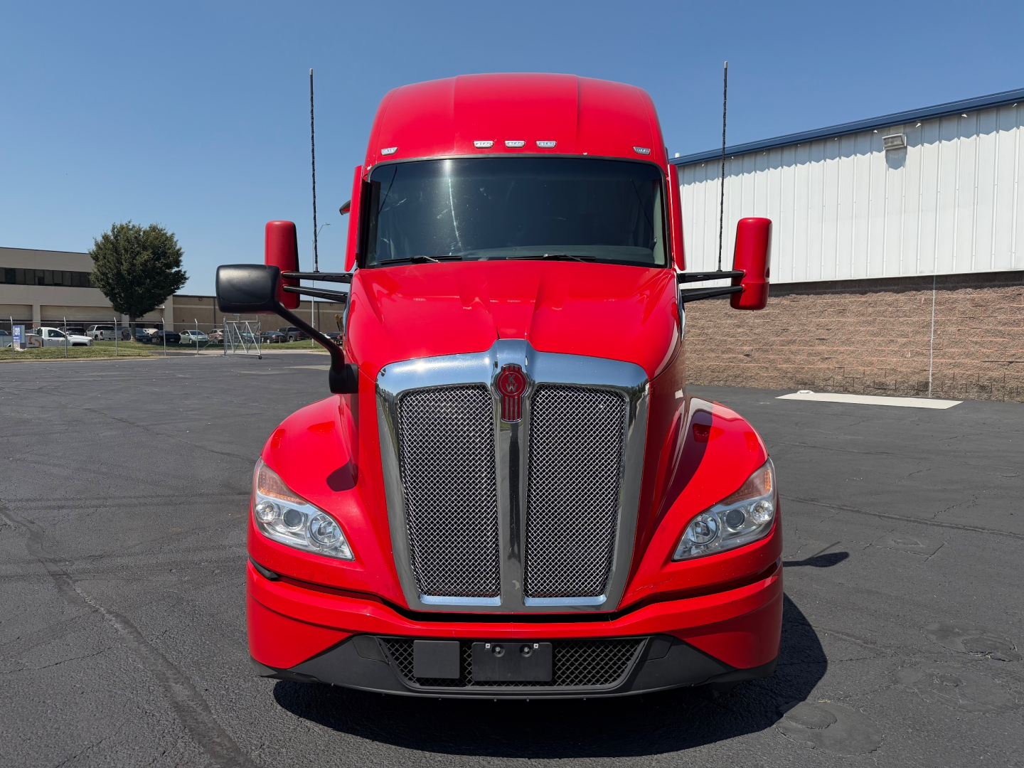 Kenworth T680 front view with bold chrome grille, red cab, and large headlights.