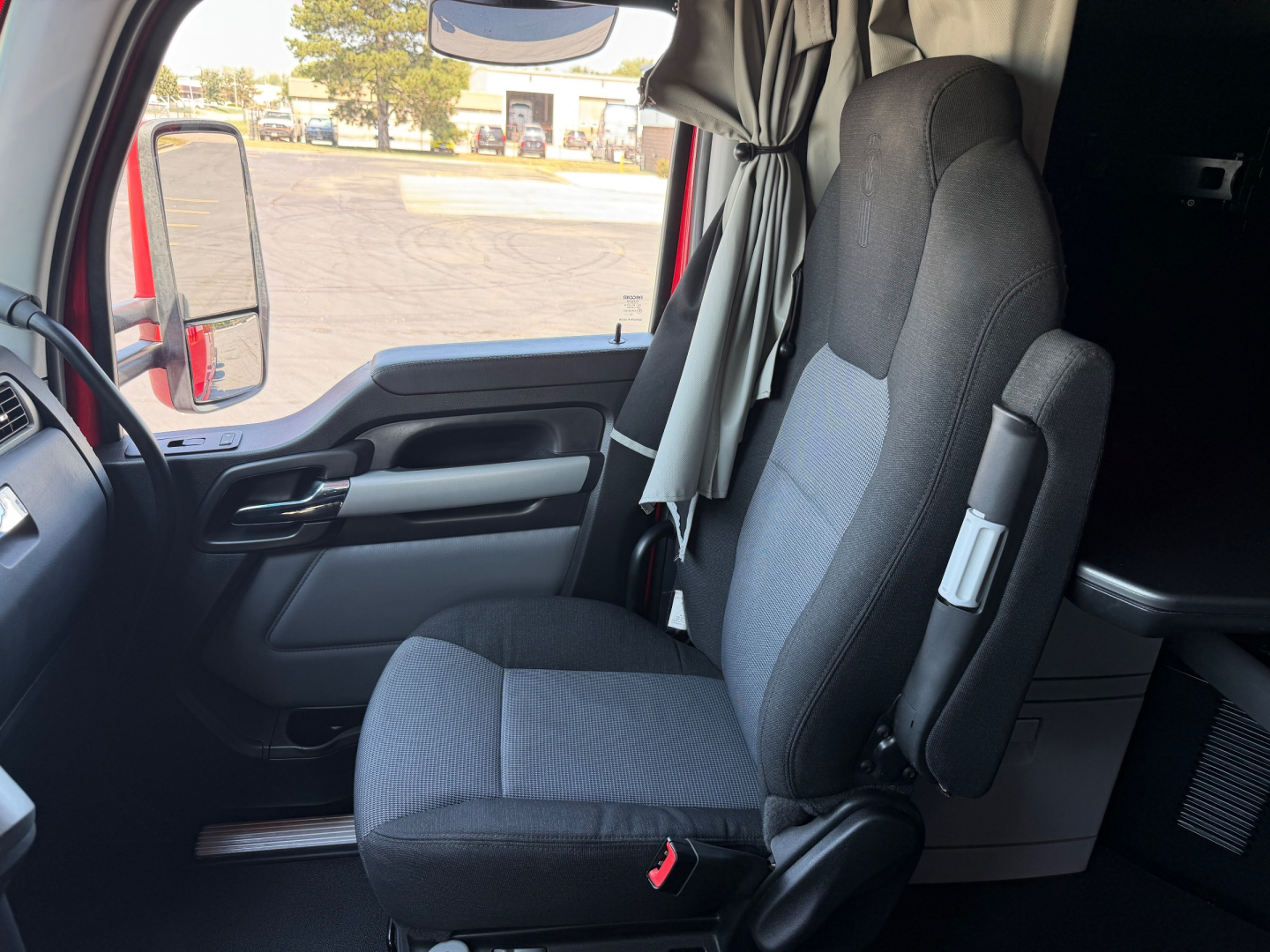 Kenworth T680 truck interior seat and door area, front cabin view from driver side with gray fabric seat and side mirror visible.