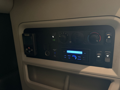 Truck cab dashboard with control knobs, radio head unit, and climate controls. Visible text on display reads 'CH' and blue-lit screen. Various buttons and dials present.