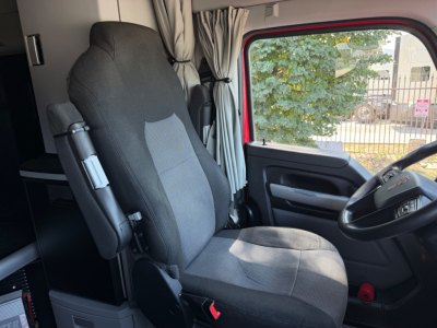 Truck cab seat and steering wheel in Kenworth T680 interior showing driver seat and window with trees outside