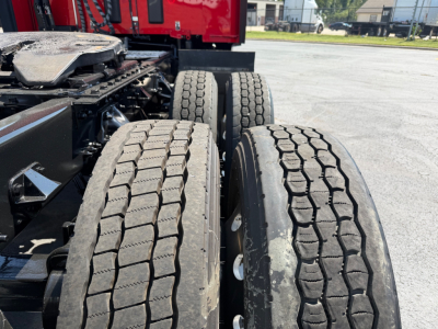 Kenworth T680 truck dual rear wheels with treaded tires and red cab visible in background, chassis and suspension components in view.
