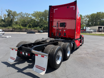 Kenworth T680 tractor rear view showing dual rear axles, mud flaps with Kenworth logo, red sleeper cab, chassis, and fifth-wheel undercarriage.