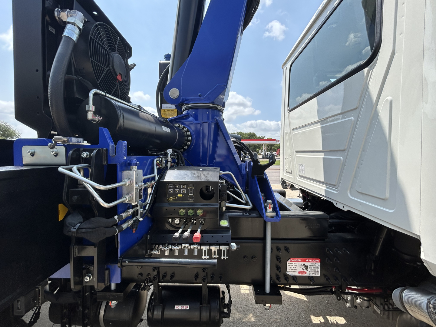 Truck cab and crane assembly showing hydraulic controls, hoses, and control panel near front of chassis; visible labels and fittings on crane base.