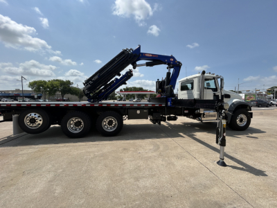 Flatbed truck with a mounted crane in transport position on a Mack GR64F chassis, long wheelbase, hydraulic crane folded over bed, crane stabilizer deployed.