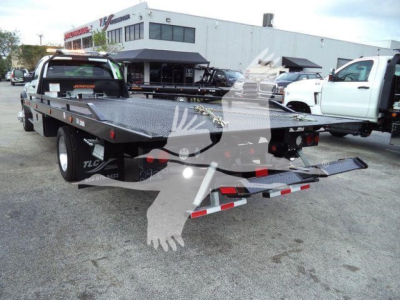 Flatbed tow truck with Ram 5500 SLT in dealership lot, rear view showing stamped metal platform and rear lights.