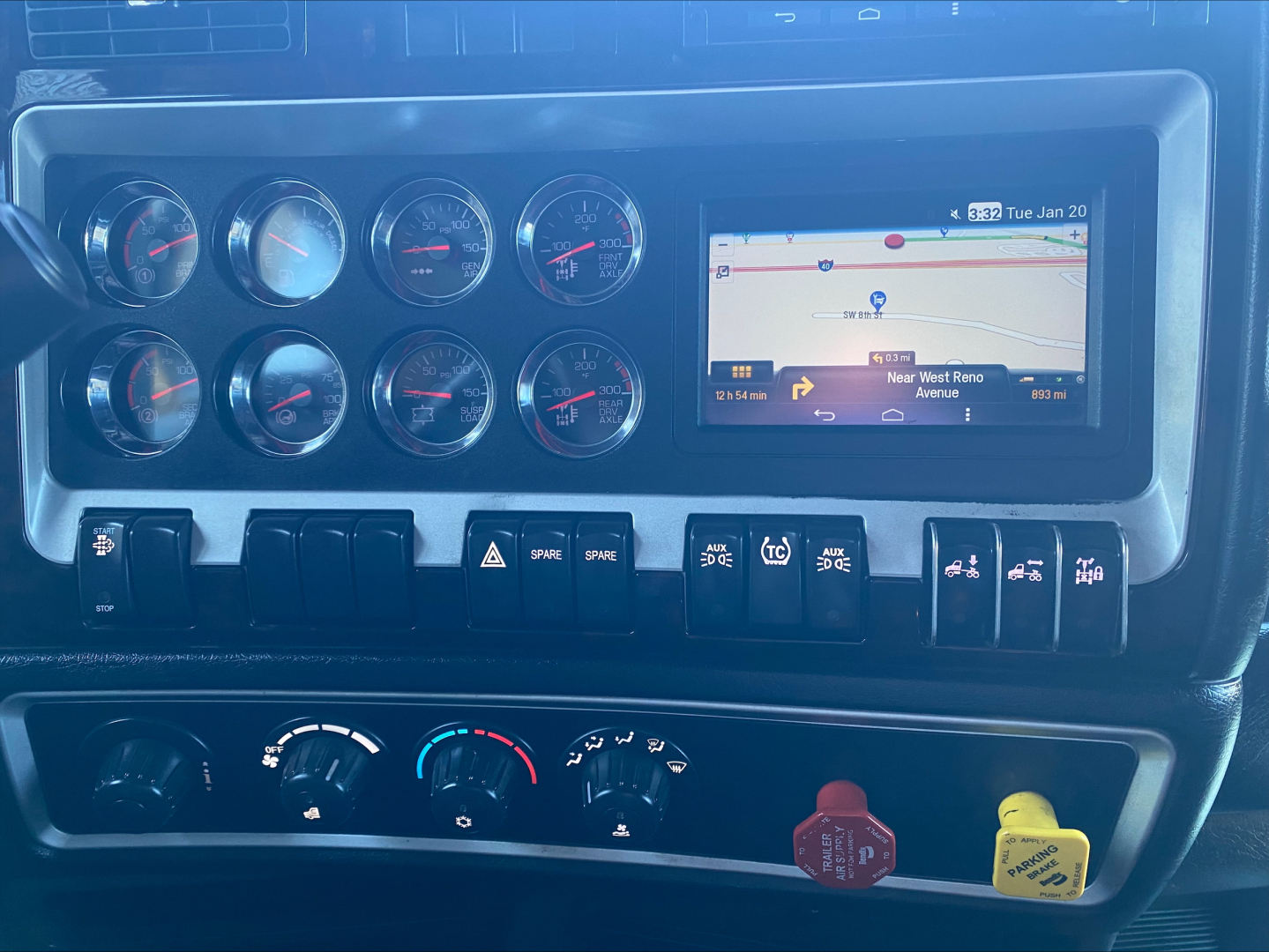 Kenworth W900L dashboard with multiple round gauges, an in-dash navigation screen, and numerous control switches.