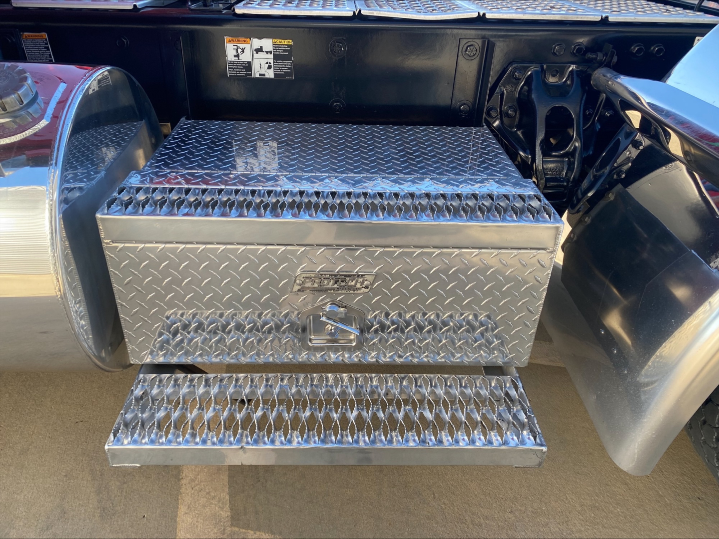 Kenworth W900L truck rear step with diamond plate toolbox and steps, showing under-truck storage box and side fuel tank area.