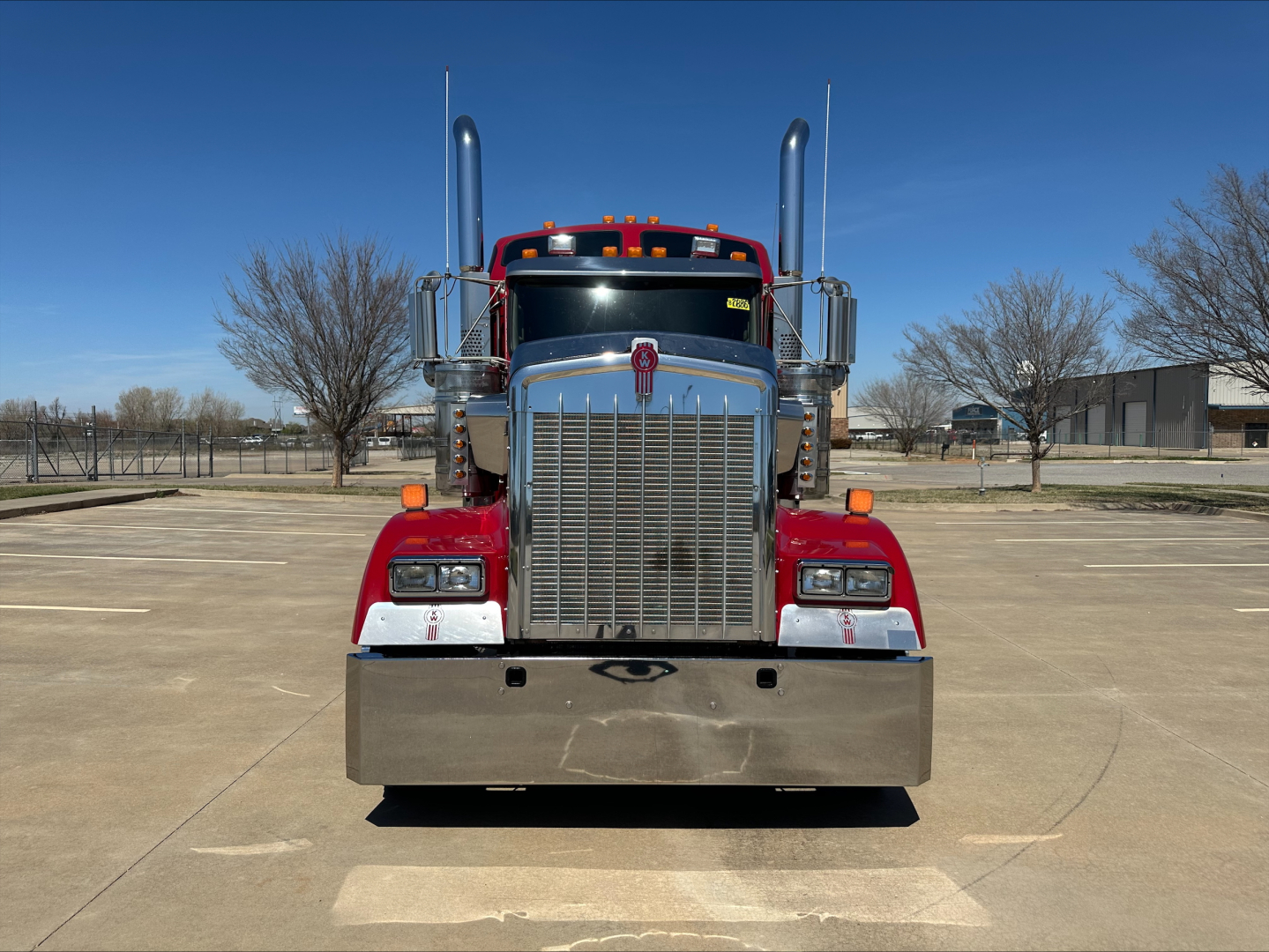 Kenworth W900L front view showing large chrome grille, dual tall exhaust stacks, red fenders, and chrome bumper.