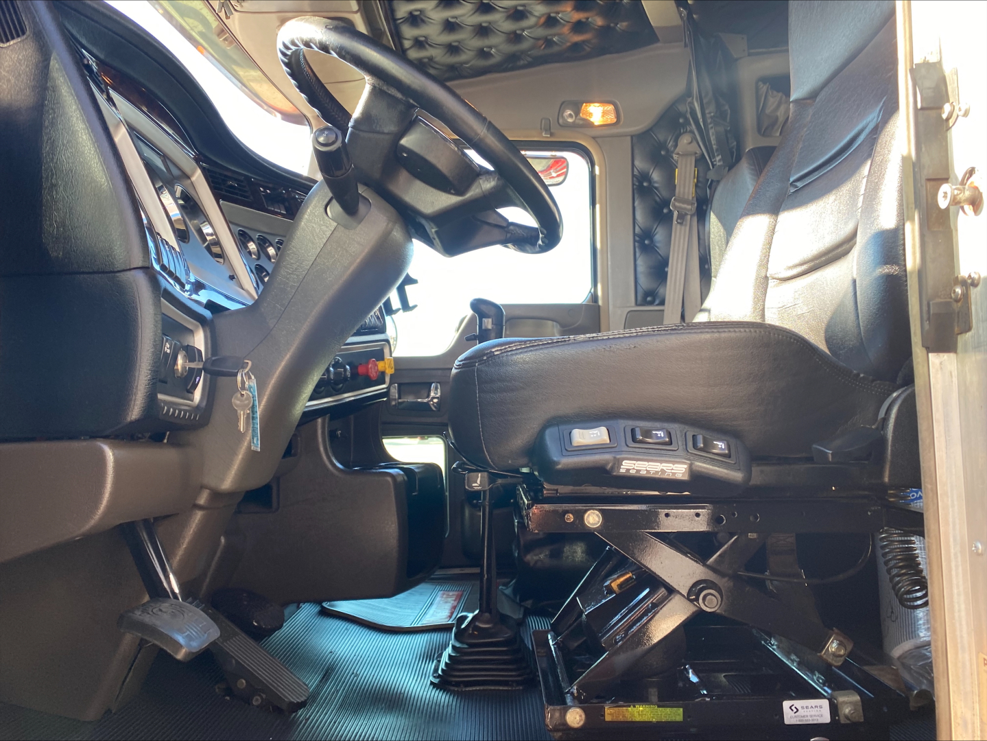 Kenworth W900L truck interior with steering wheel, driver seat controls, and dashboard visible.
