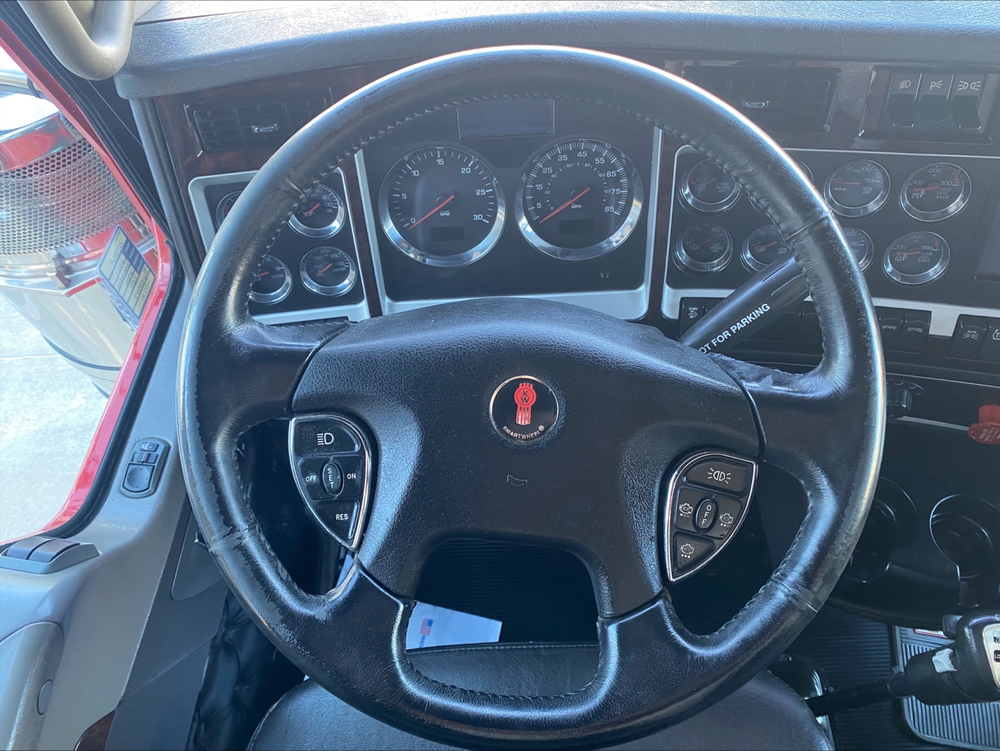 Kenworth W900L truck interior showing steering wheel with Kenworth emblem, gauge cluster, and dashboard controls.