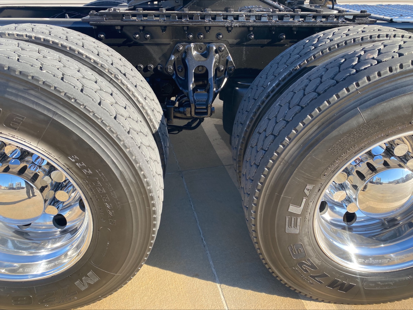 Kenworth W900L rear/central chassis showing dual rear axles and suspension with chrome wheels and tires; no readable text visible on components.