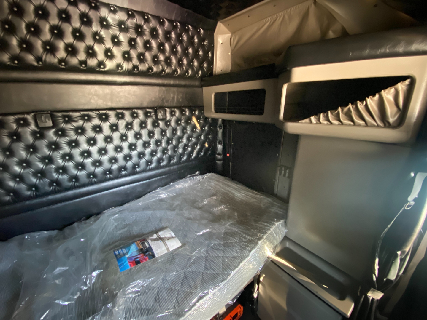 Kenworth W900L sleeper cab interior showing bunk bed area with diamond-tufted upholstery and storage shelves.