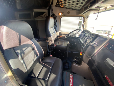 Kenworth W900L cabin interior showing driver and passenger seats, steering wheel, and dashboard with gear shifter and controls.