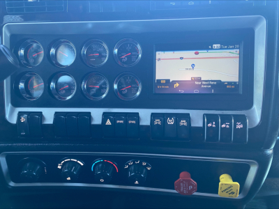 Kenworth W900L dashboard with multiple round gauges, an in-dash navigation screen, and numerous control switches.