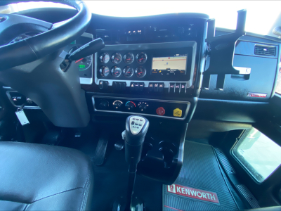 Kenworth W900L truck interior dashboard and gear shifter showing steering wheel, instrument cluster, GPS display, control switches, and Kenworth-branded floor mat.