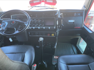Interior of a 2021 Kenworth W900L cab with manual gear shifter, dashboard controls, steering wheel, and seats visible.