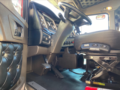 Interior of a Kenworth W900L truck driver area showing steering wheel, dash, and adjustable seat with controls.