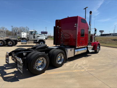 Kenworth W900L tractor cab in a parking lot, rear shows dual rear axles and fifth-wheel, red cab with chrome exhaust stacks.