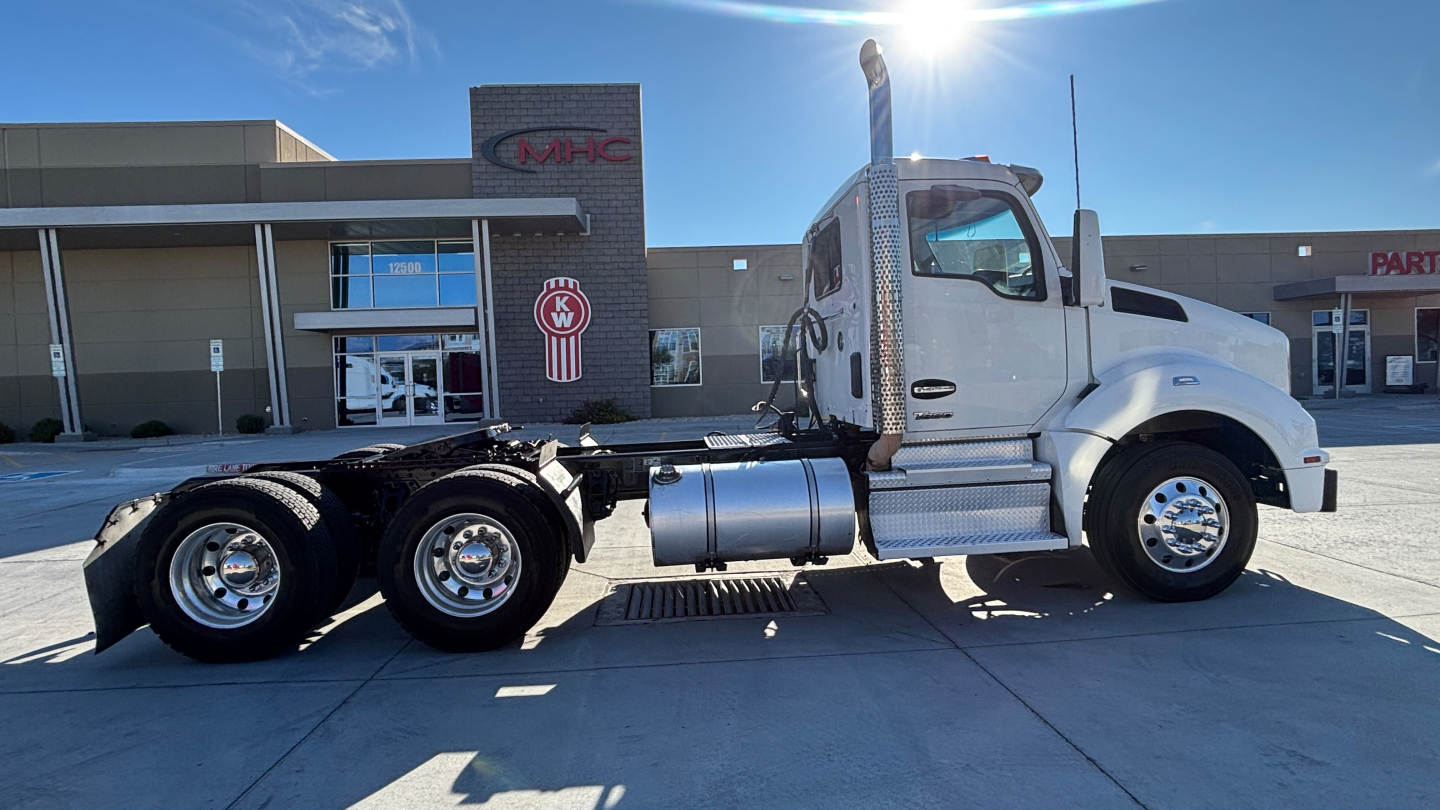 Kenworth T880 conventional daycab tractor tractor-trailer missing trailer shown in daylight rear three-quarter view white cab chrome fuel tanks and dual rear axles