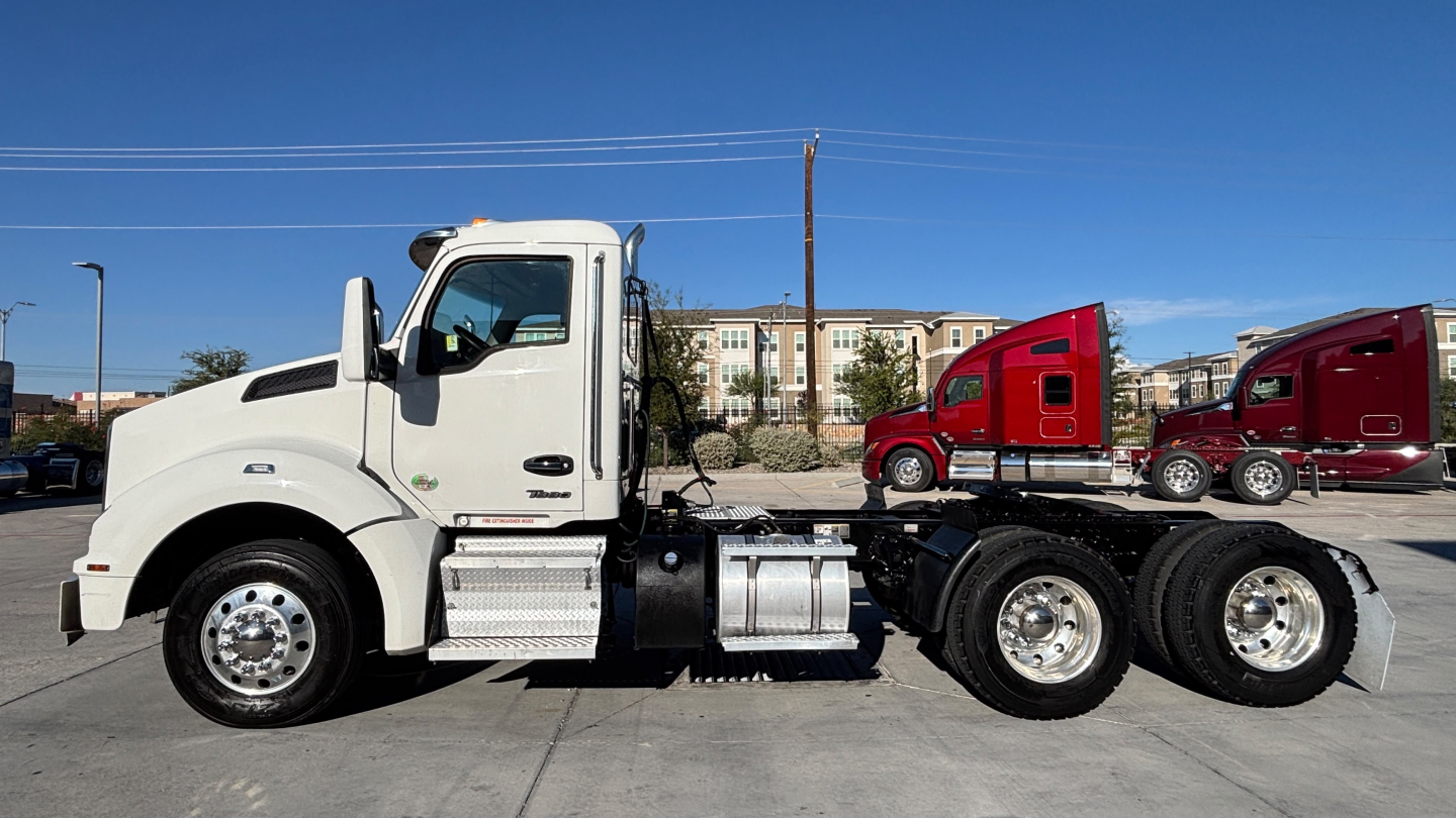 Kenworth T880 Conventional Daycab tractor seen in profile, white cab, chrome fuel tanks, dual rear axles, side view with attached trailer hitch area visible.