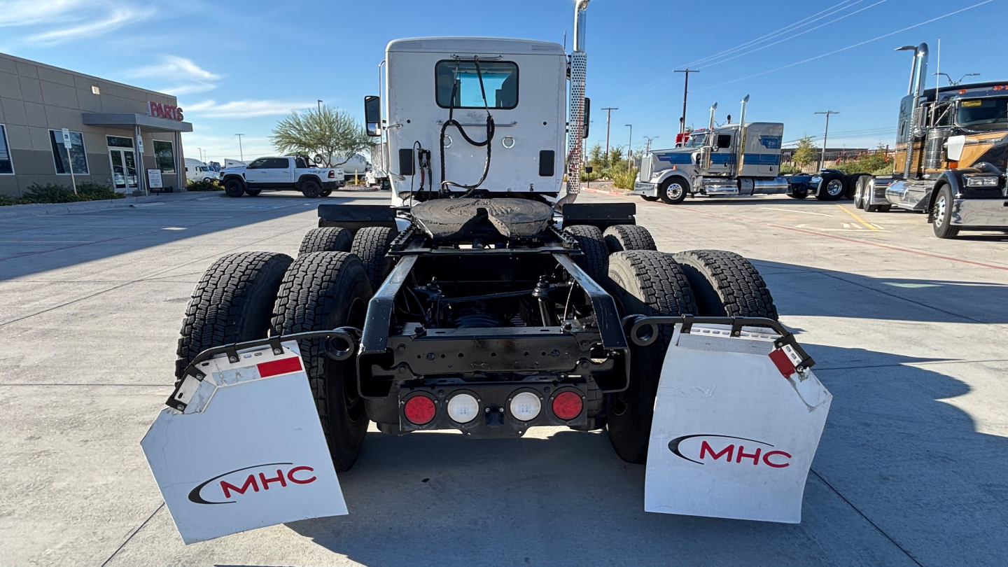 Truck chassis rear view showing dual rear axles and mud flaps with MHC logos, chassis frame and fifth-wheel area visible.