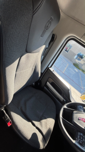 Truck cab interior showing driver's seat and steering wheel with Kenworth emblem; window view of exterior; no additional text visible.