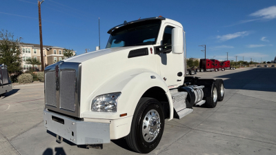 Kenworth T880 conventional daycab truck in white, side view, showing front grille, headlights, and cab with fuel tanks; clear blue sky.