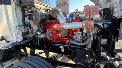 Kenworth T880 engine bay with red engine block, hoses, and components visible; exhaust and chassis framing in view.