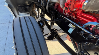 Kenworth T880 engine bay area showing frame rails and a red engine component with hoses and a black suspension link.