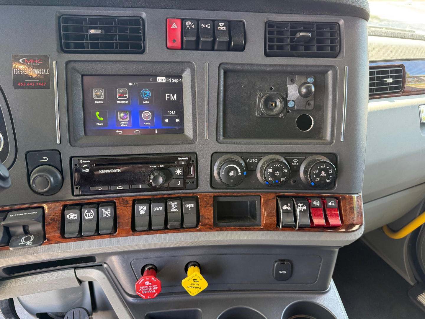 Kenworth T680 cabin dashboard with touchscreen infotainment, climate gauges, switches, and ignition area visible.