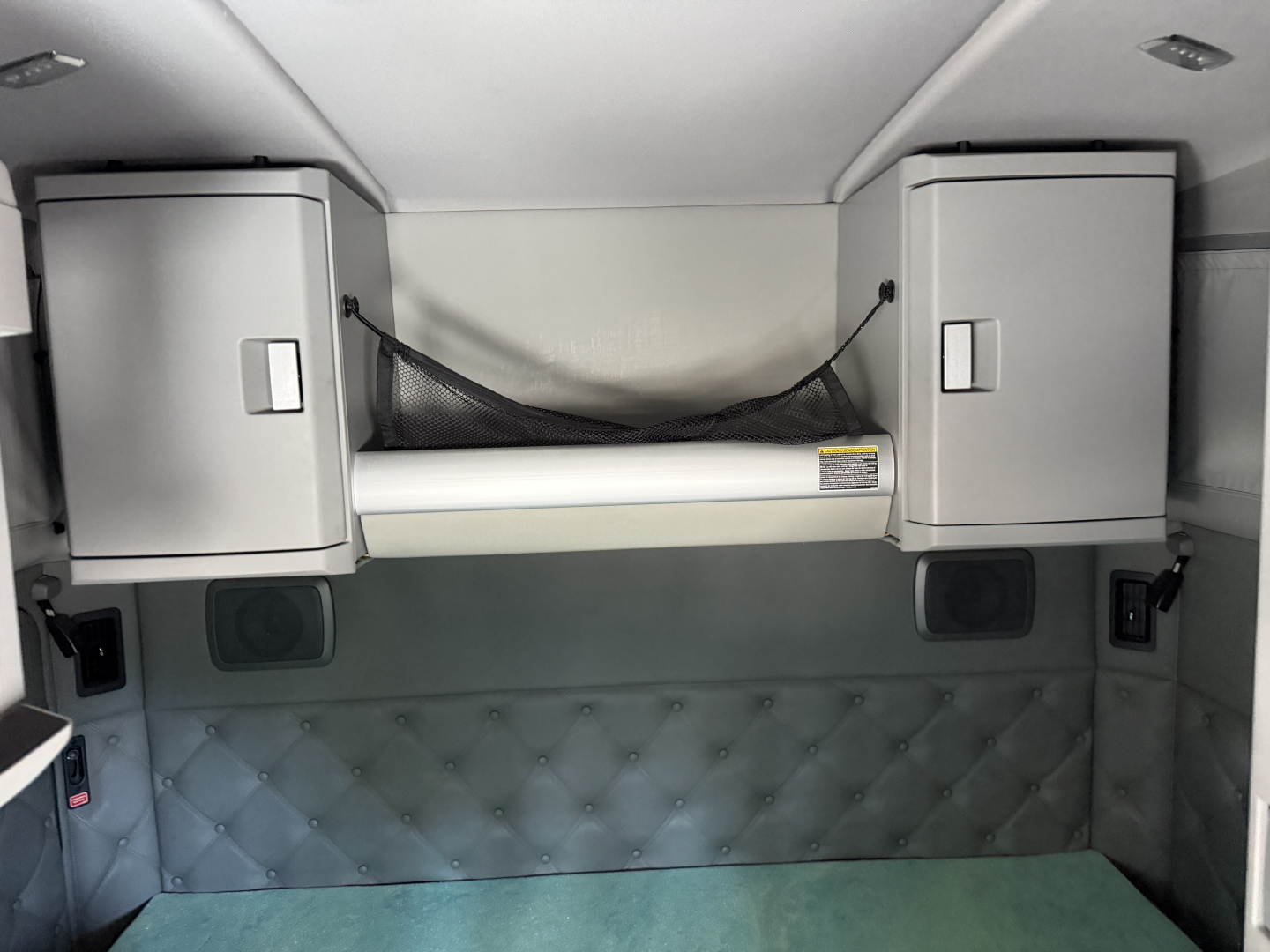 Kenworth truck sleeper cab interior with bunk area, overhead cabinets on both sides and a horizontal bar in the middle; quilted wall paneling.