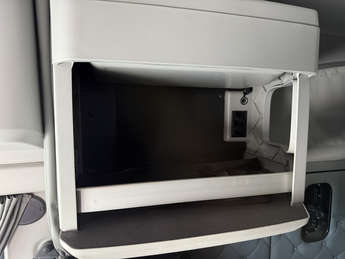 Kenworth T680 sleeper cab front storage compartment open showing interior dash area and electrical outlet.