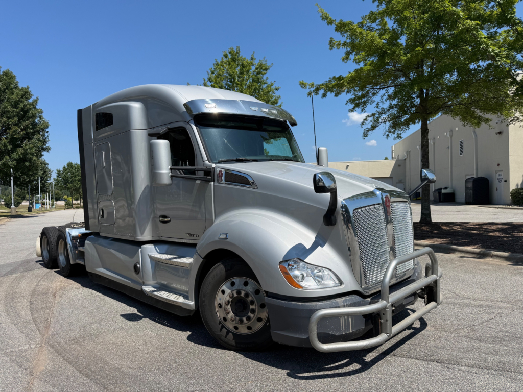 Kenworth T680 tractor-trailer cab with chrome grille guard, silver paint, side fuel tanks. Visible text: no legible serials or labels clearly readable in image.