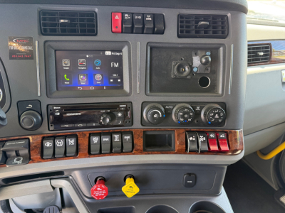 Kenworth T680 cabin dashboard with touchscreen infotainment, climate gauges, switches, and ignition area visible.