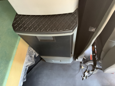 Cab interior showing a storage cabinet with a diamond-pattern black top and light gray body, near a passenger seat and a coiled cord.
