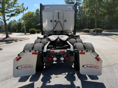Kenworth T680 rear view showing dual rear axles with mud flaps and fifth wheel, stock number tag visible, road in background.