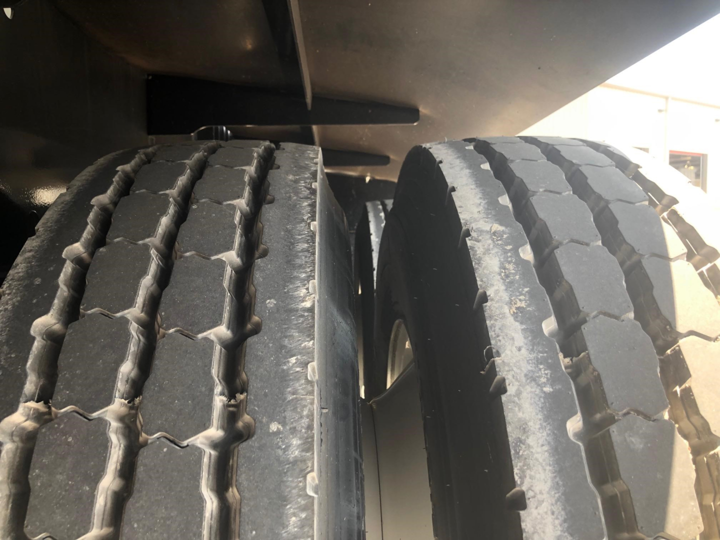 Dual semi-trailer tires and undercarriage seen from side showing tread on tires.