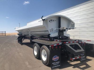 Side-dump trailer on dual-axle setup with Jet logo, white exterior, and hydraulic dump bed mounted on a flatbed trailer.