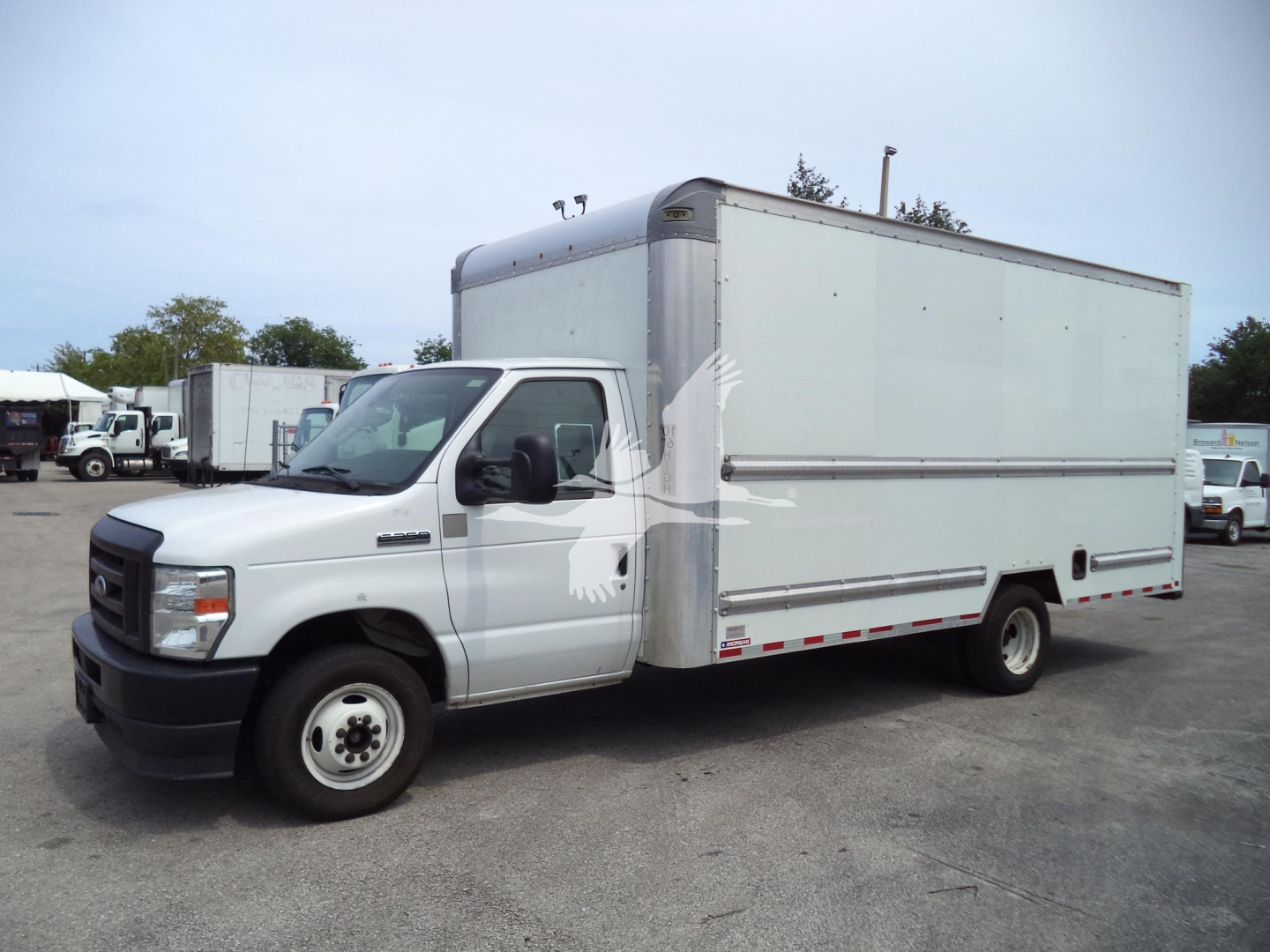 Ford E-350 box truck in a used fleet lot. White cab with large rectangular box cargo area, side mirrors, and standard steel wheels.