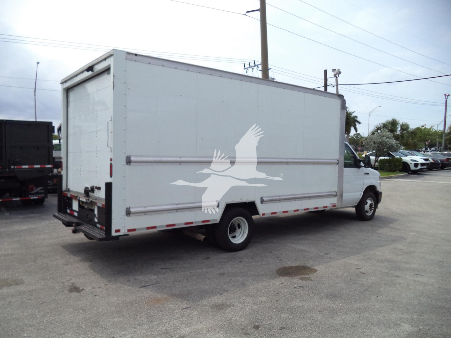 Ford E-350 box truck with cargo body, rear Roll-up door, white paint, logo of a bird on side, side view showing cargo box and truck cab.