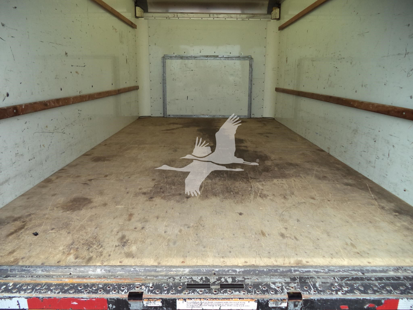 Interior of a cargo box (empty) with a wooden floor and faint logo of a flying bird on the surface.
