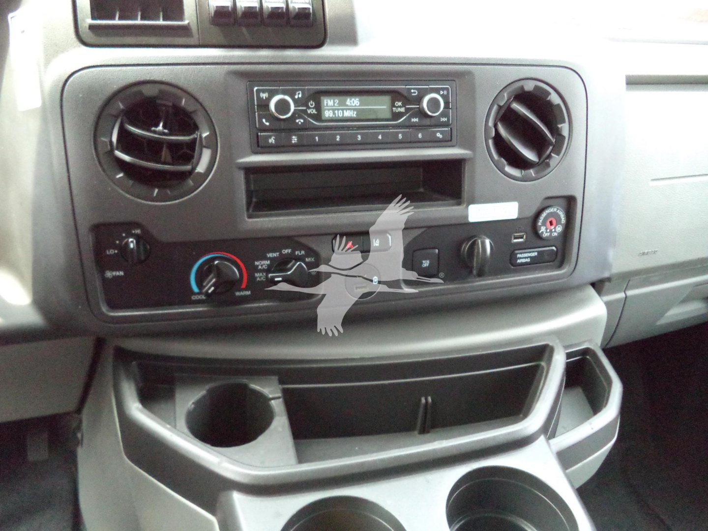 Ford E350 dash area showing factory radio, two circular air vents, climate controls, and lower storage compartments.