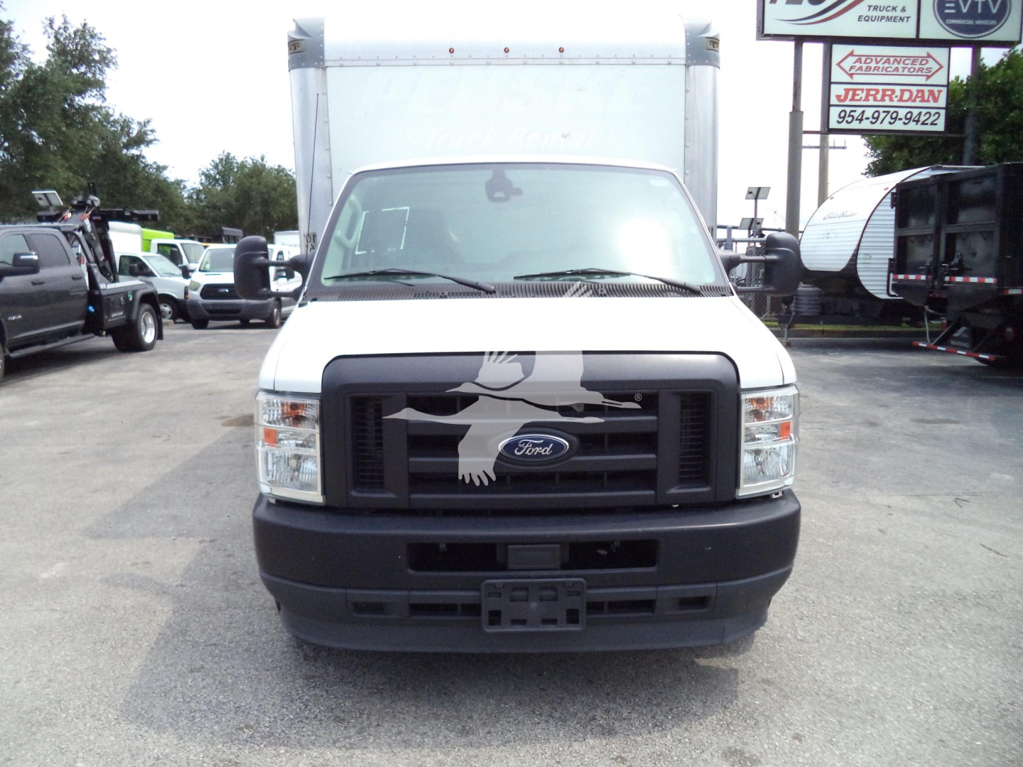 Ford E-350 front view showing black grille with Ford emblem, large cargo box in background, daytime dealership lot with other vehicles