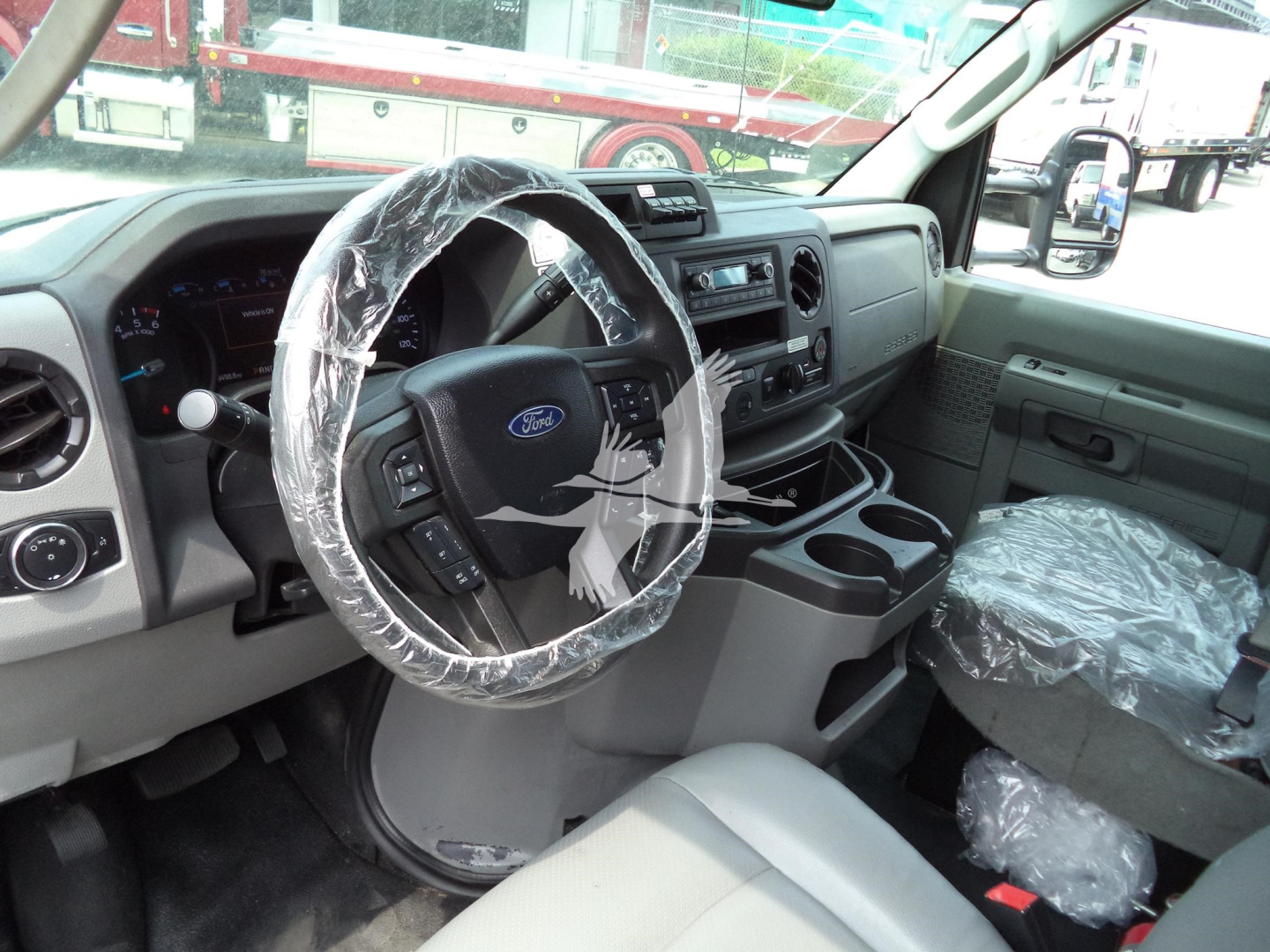 Ford E-350 van interior showing steering wheel with plastic cover and dashboard, front seats wrapped in protective plastic.
