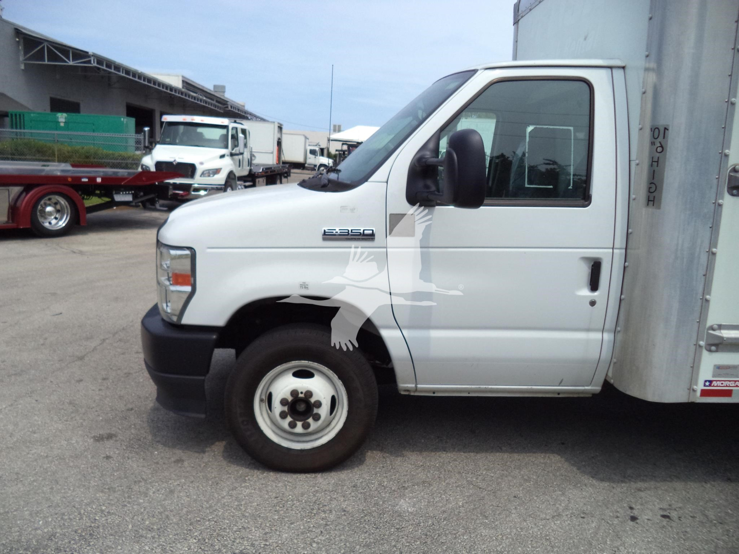 Side view of a white Ford E-350 cutaway/box truck showing front wheel, cab, and cargo box with some text on the door window.
