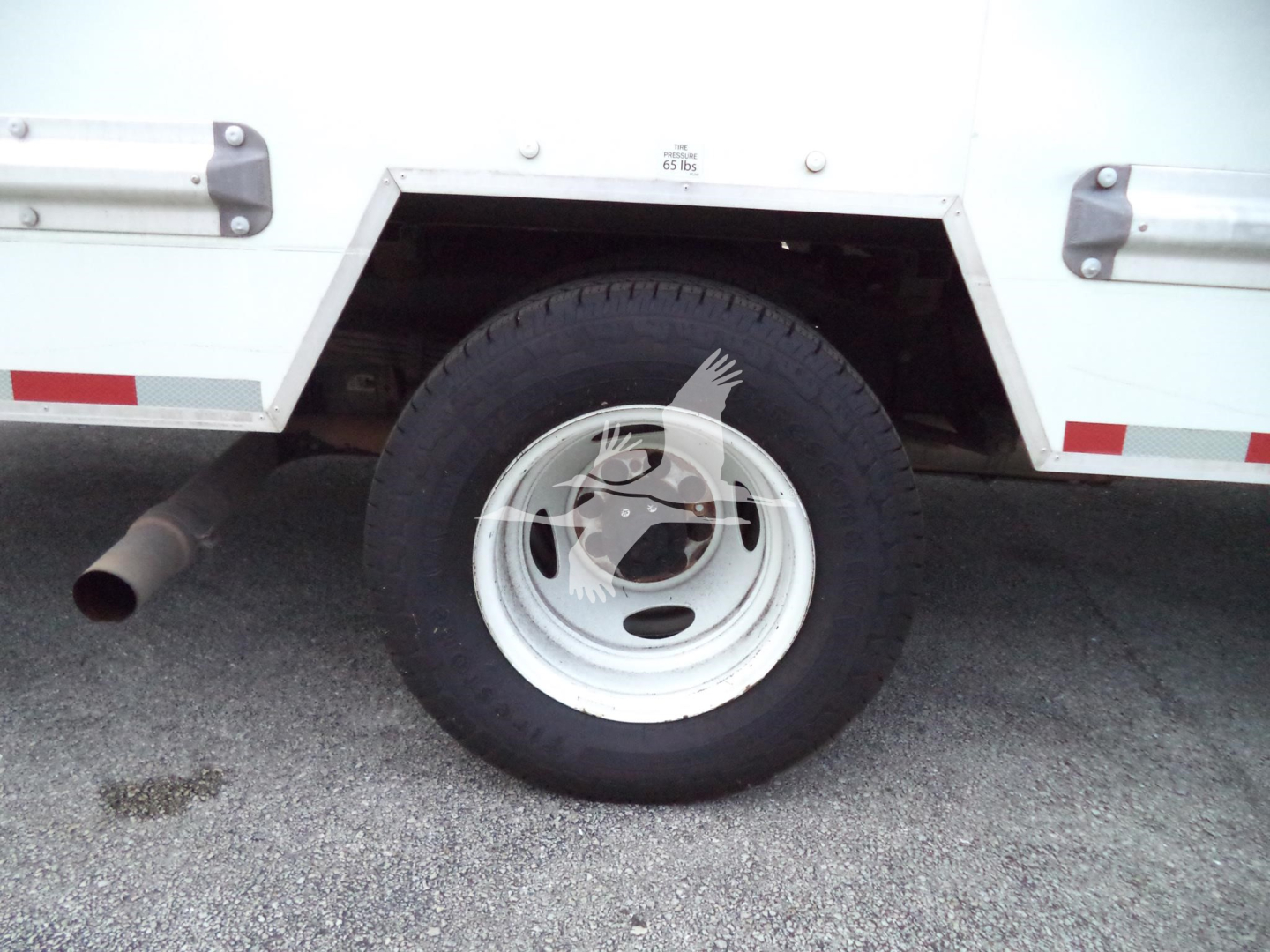 Truck wheel and rear side of a 2022 Ford E350 cargo box with white painted wheel, side step and exhaust visible.